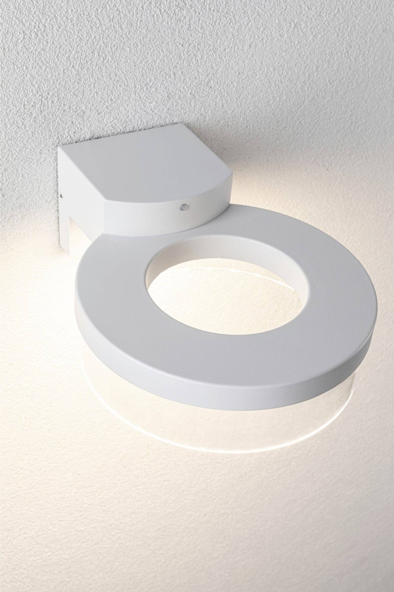 A round, contemporary wall light with a circular illumination cast on a white wall surface.
