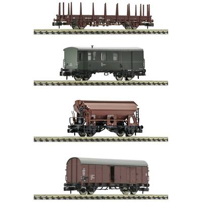 Four model railway goods wagons on tracks: an open timber transporter, a green luggage van, a bulk goods wagon, and an enclosed goods wagon.