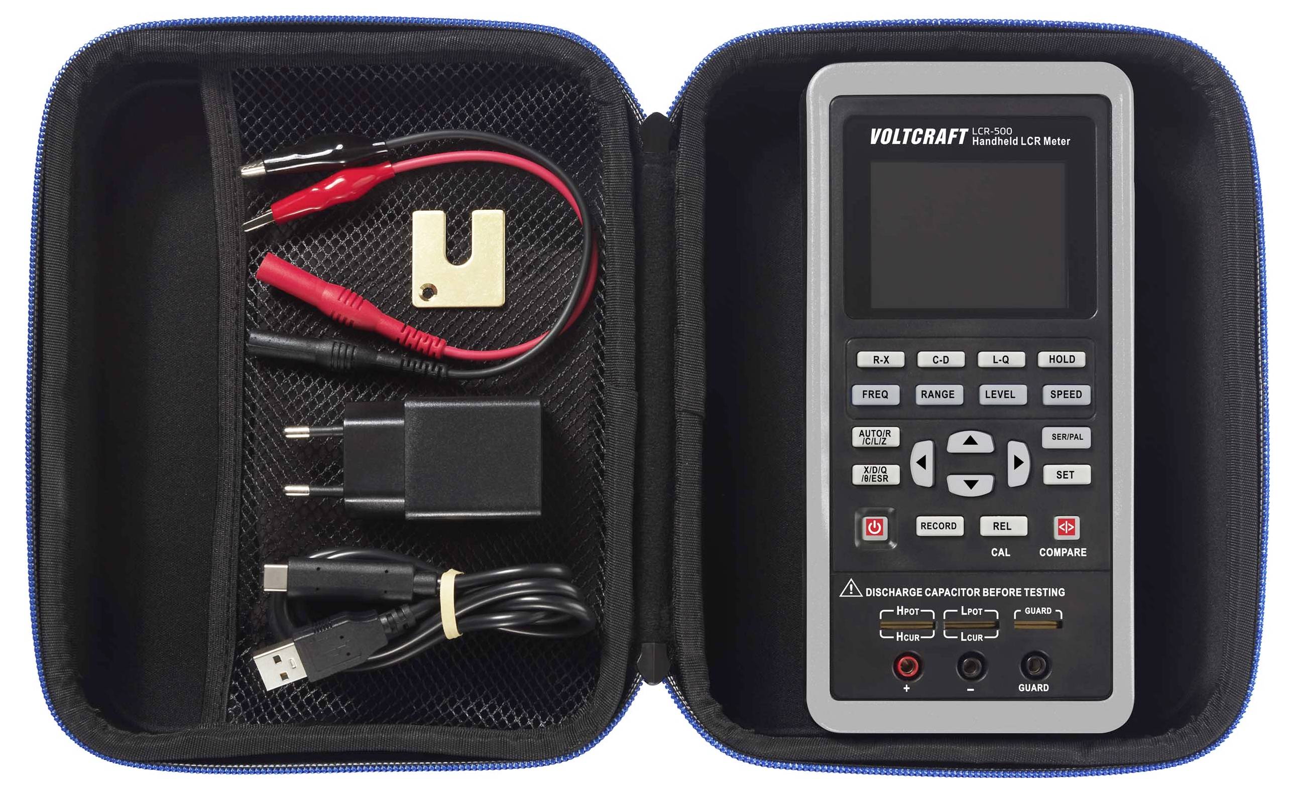 A portable LCR measuring device in an open protective case. On the left are measurement cables and charging accessories.