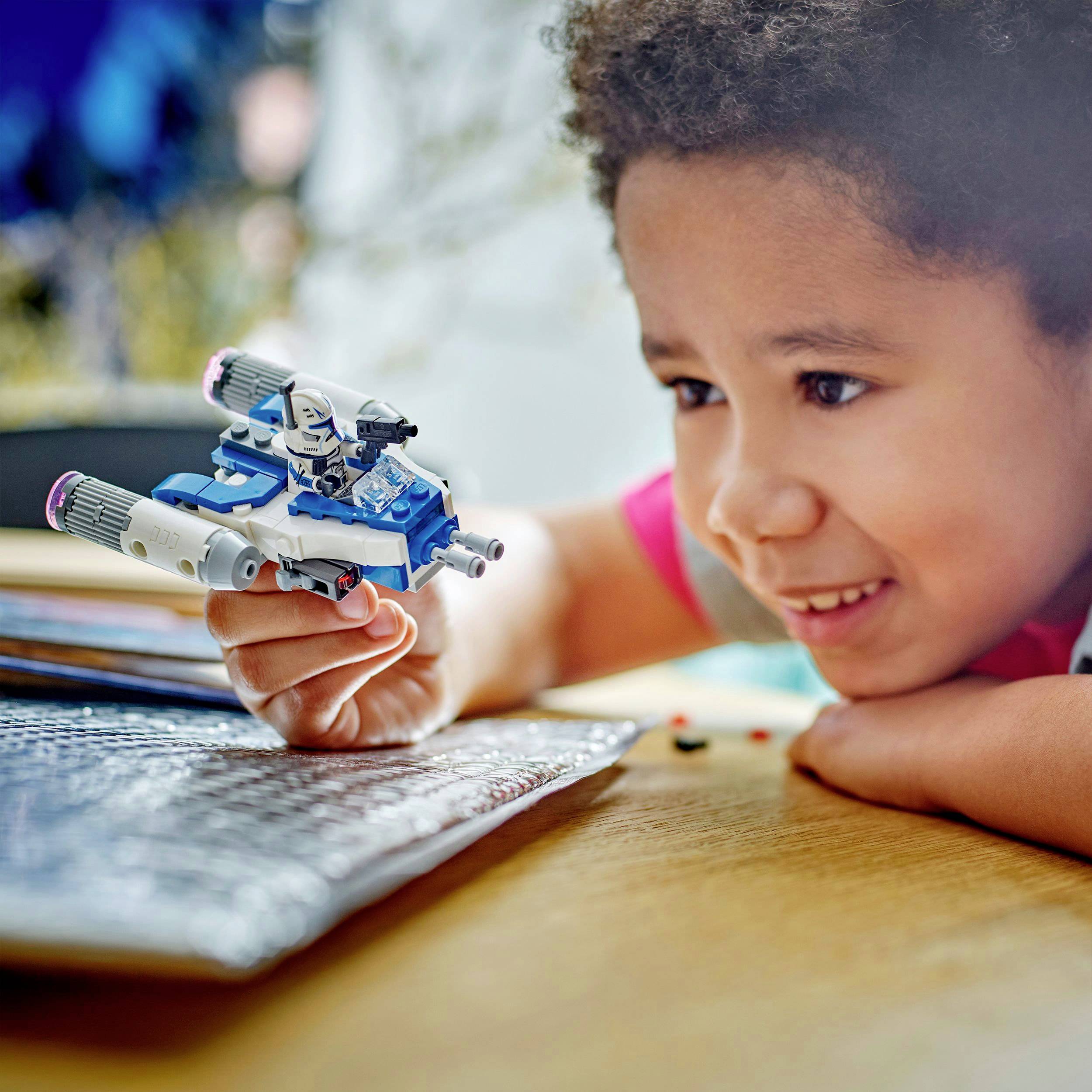 A child is happily playing with a small, white and blue spaceship toy, holding it above a table.