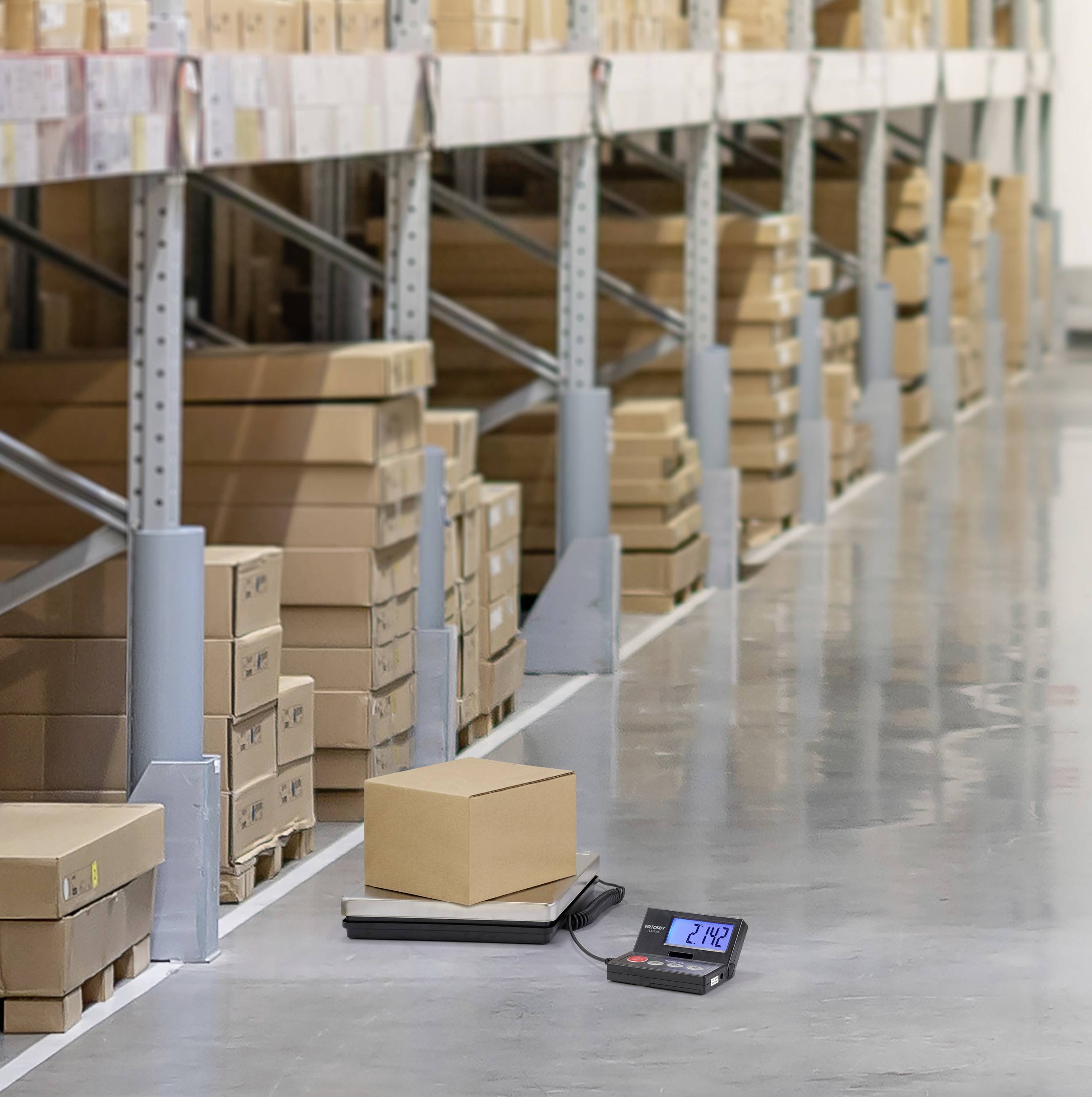 A cardboard box is being weighed on an electronic scale in a warehouse. In the background, numerous other boxes are stacked on shelves.