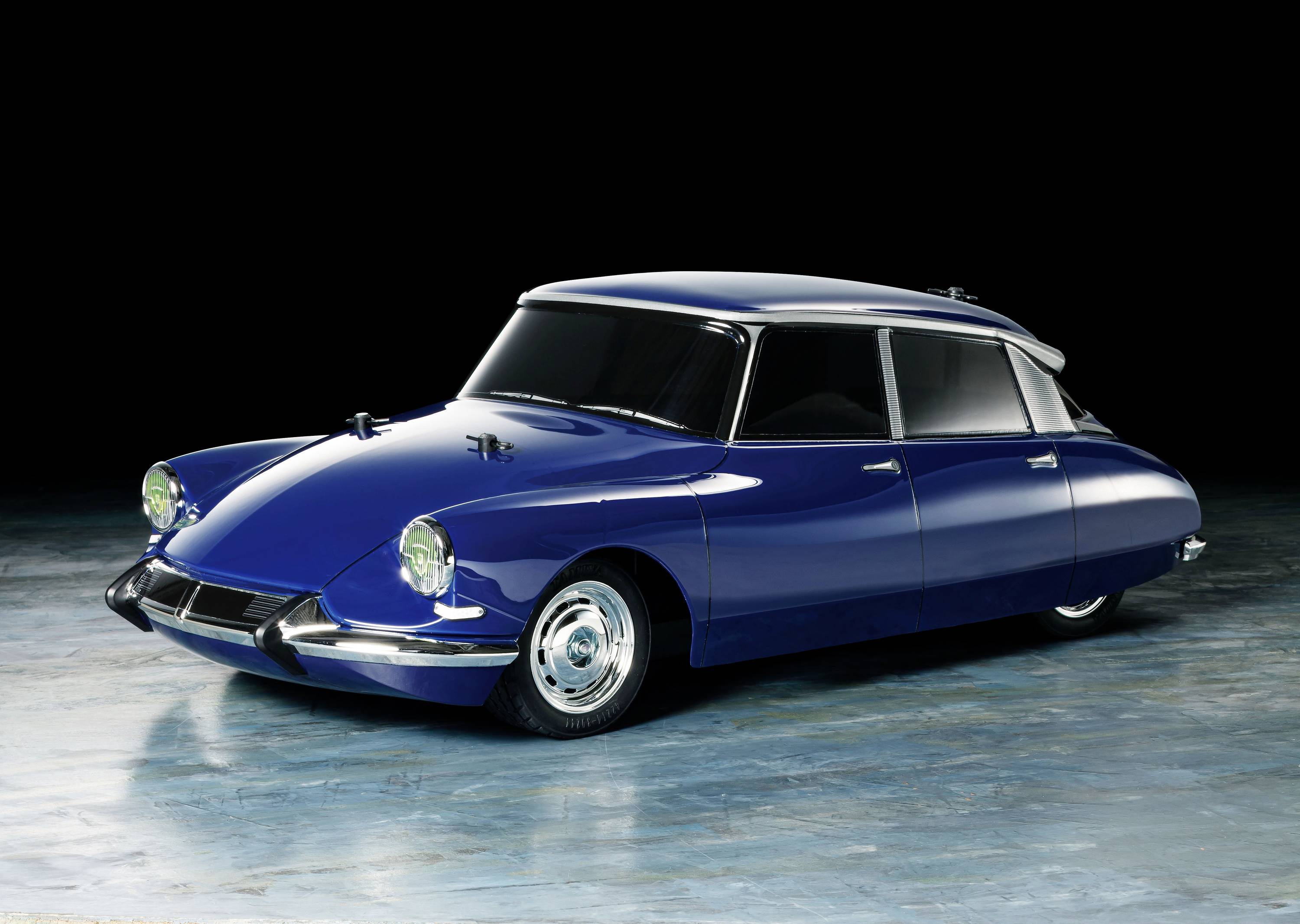 A blue vintage car with characteristic round headlamps and a curved design stands on a reflective floor.