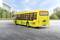 A yellow toy bus with stickers is parked on a road. Blurry buildings and trees are visible in the background.