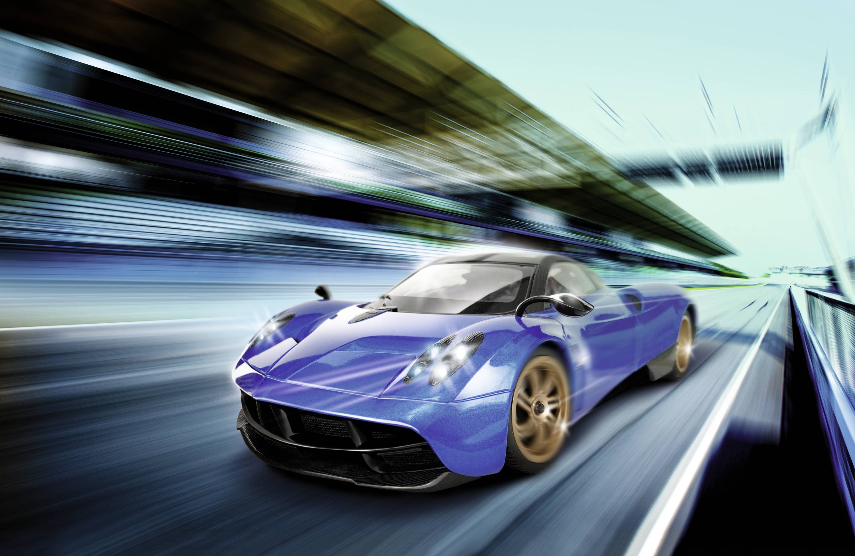 A blue sports car speeds along a racing circuit, surrounded by blurred grandstands and track boundaries.
