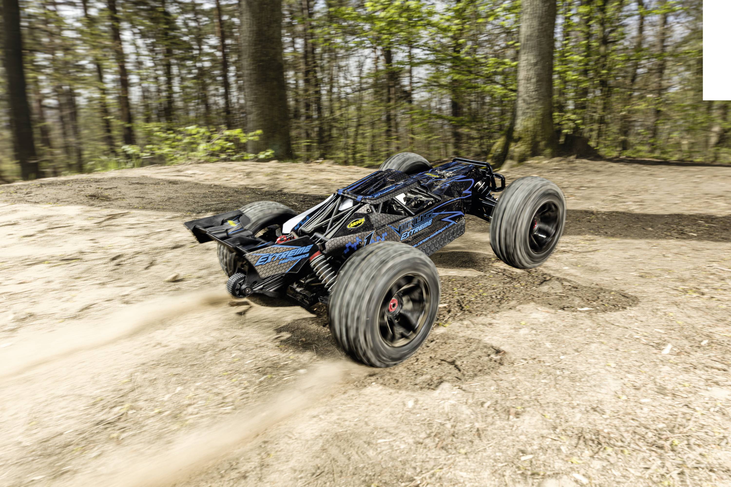 A remote-controlled car speeds along a forest path. Dust billows up behind its large tyres.