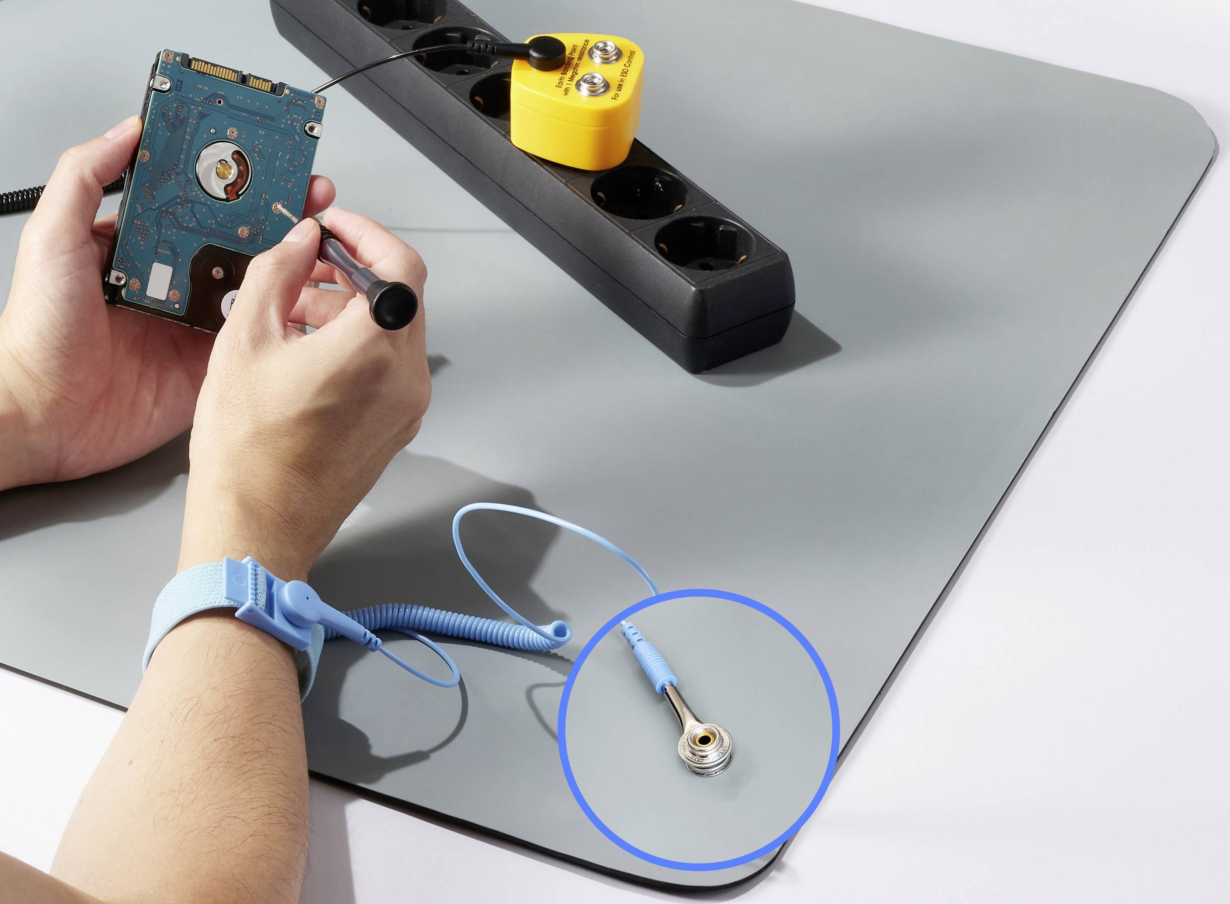 A person is working on a computer hard drive on an anti-static mat. A blue grounding wristband is visible.