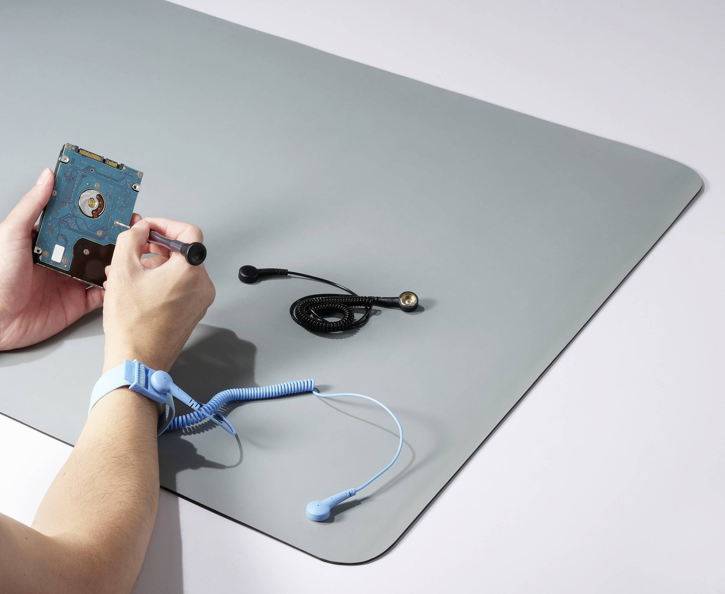 A person is repairing a hard drive with a screwdriver on an anti-static mat. An earth strap is attached to their wrist.