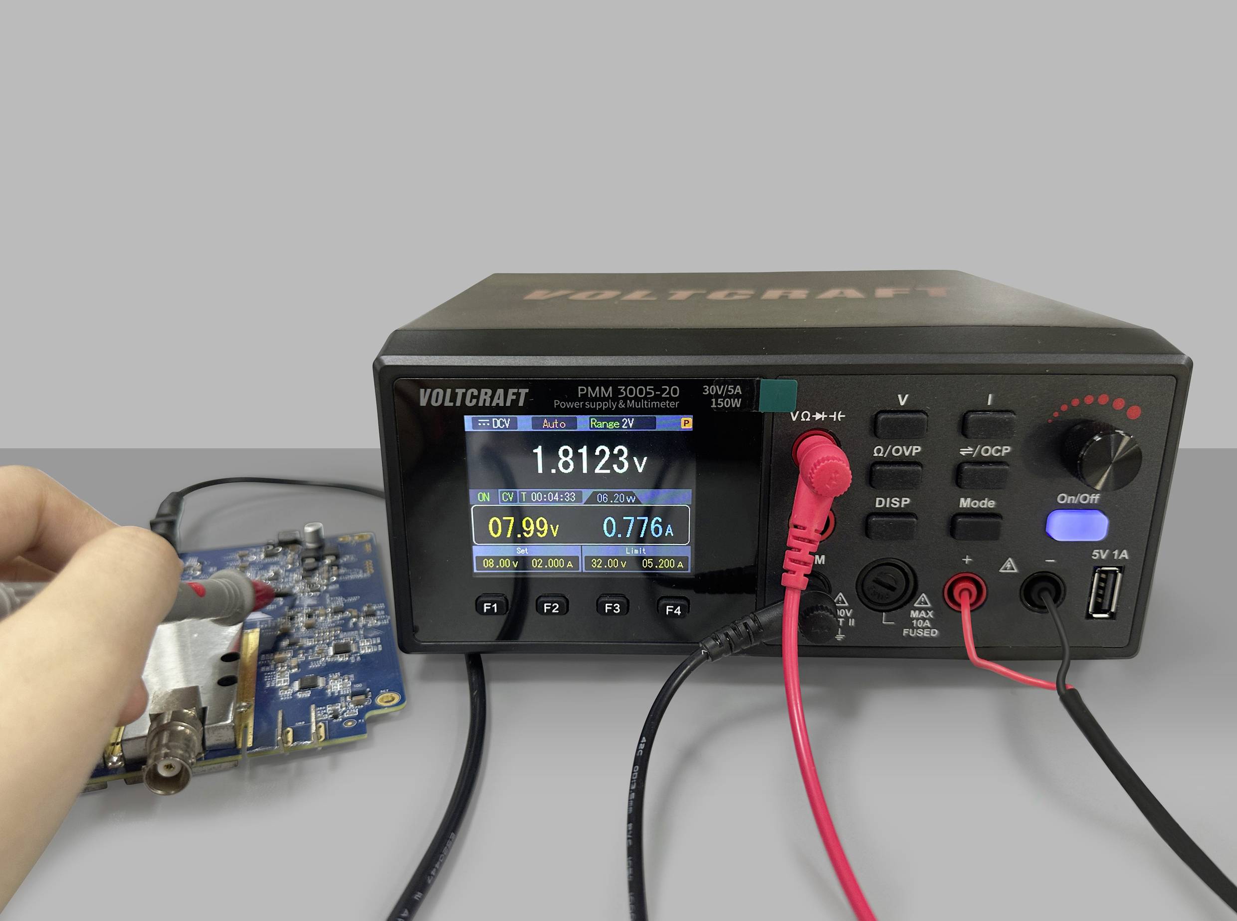 A measuring device shows '1.8123 V' and '0.776 A' on a digital display, while a hand tests the voltage on a circuit board.