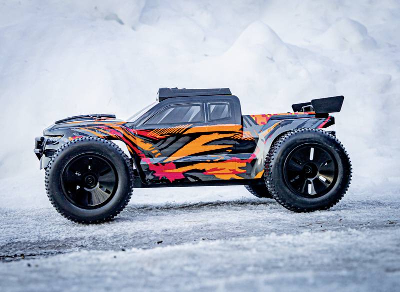 A remote-controlled car with a glowing pattern stands on snow and ice. A snowy landscape is visible in the background.