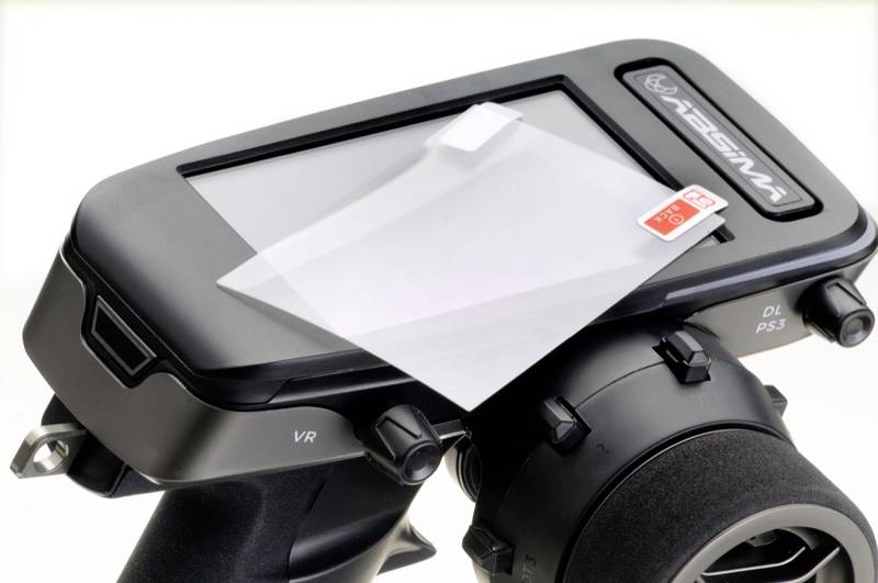 A black device with a screen, on which a translucent protective film with a red label rests. Some buttons for control are located on the left.