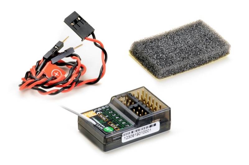 A small electronic module with multiple slots and labelling, two cables with plugs, and a rectangular sponge.