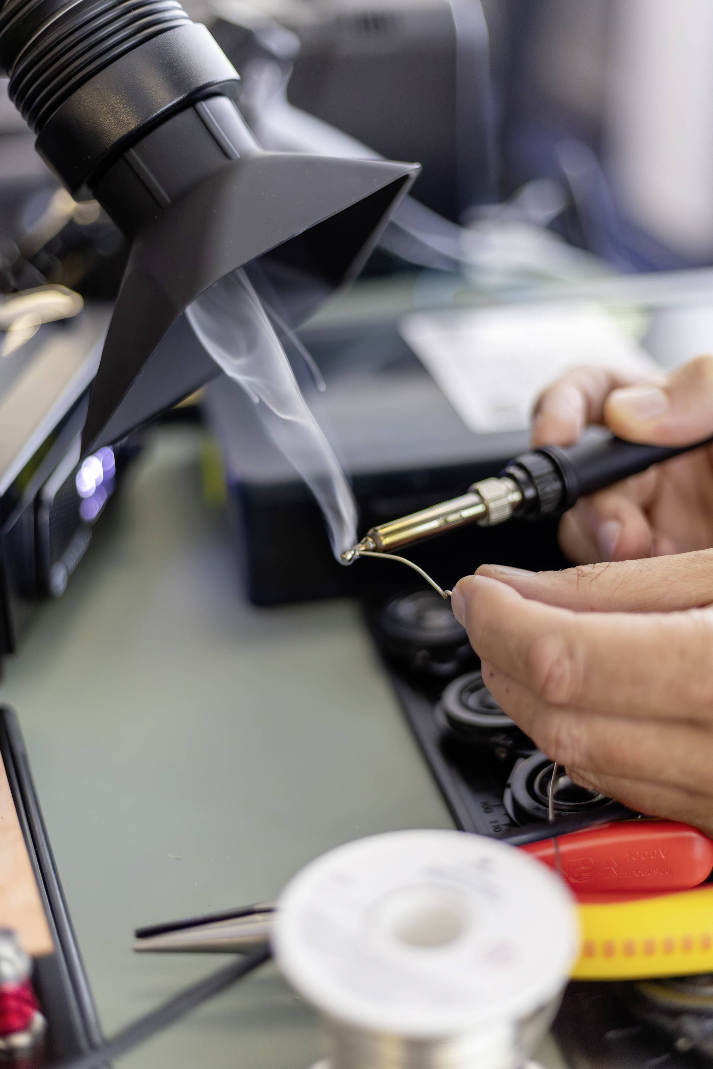 Close-up of a person soldering electronics with a hot-air tool and soldering iron at a workbench.
