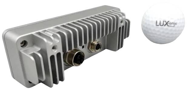 Metallic, rectangular electronic sensor with cooling fins and two plug connectors. To the right, a golf ball with 'LUXonis' printed on it.