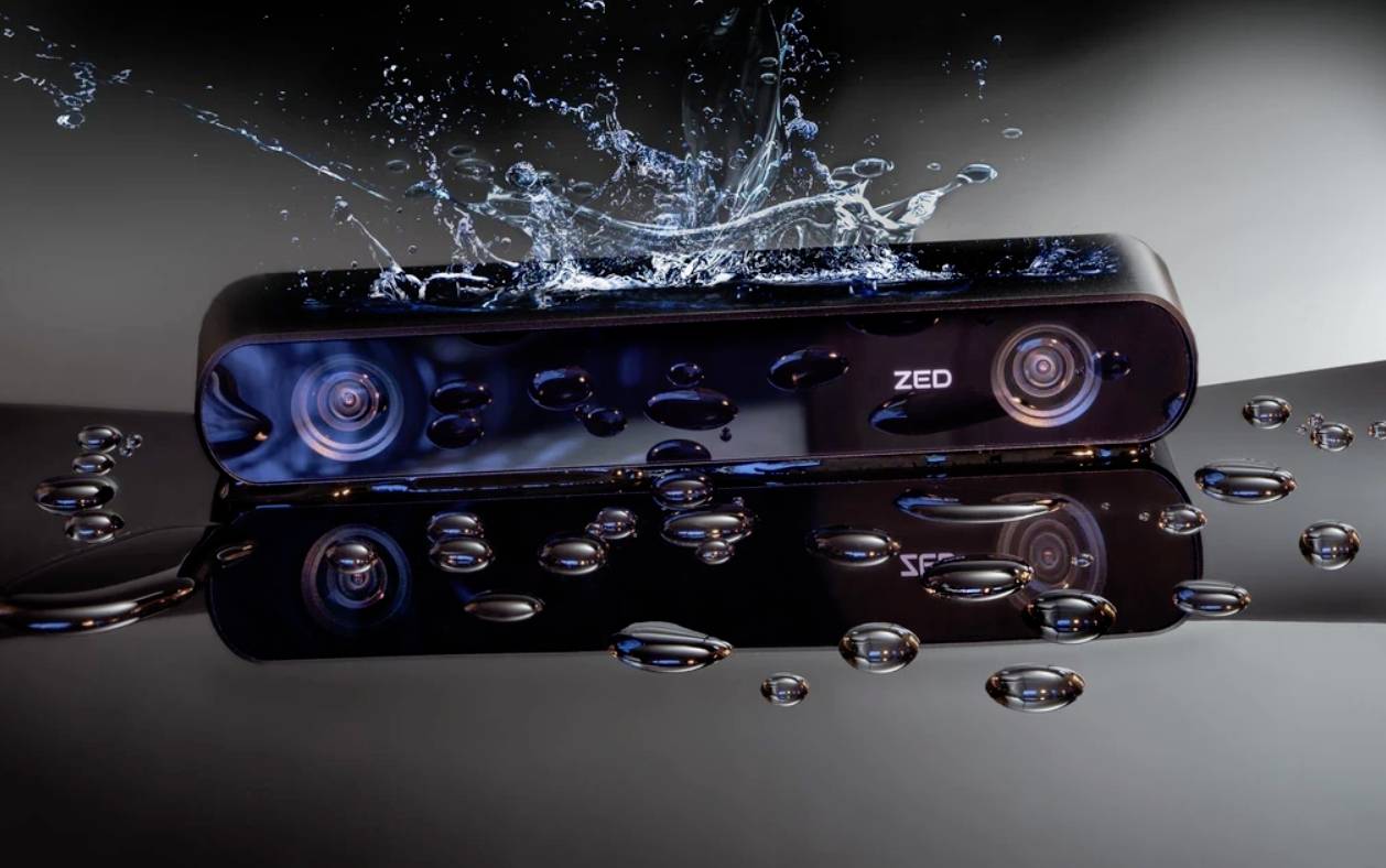 A black camera with two lenses, labelled 'ZED', is surrounded by splashing water, suggesting its water resistance.