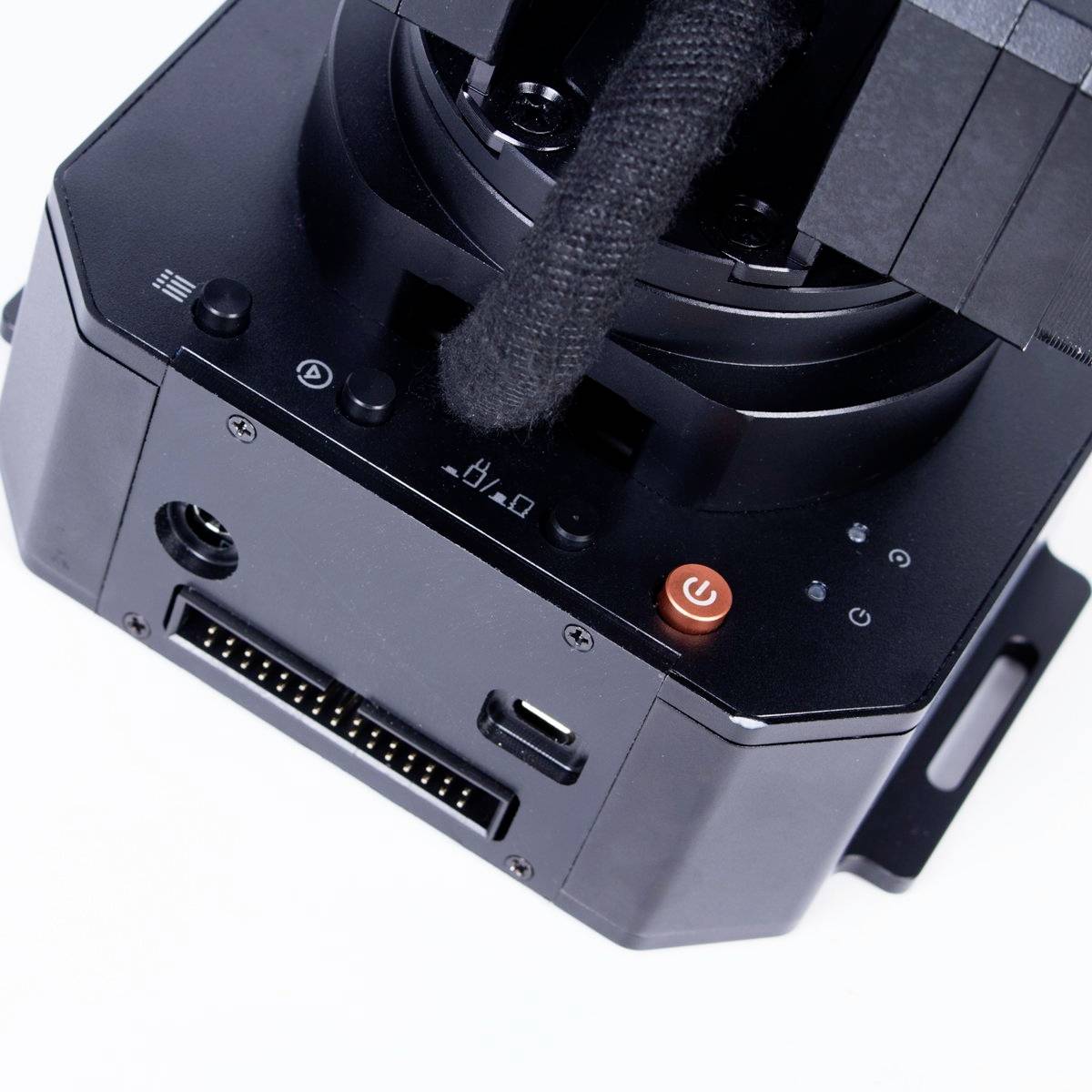 Black technical device viewed from close up, with buttons and connections visible. The main feature is a red illuminated power button.