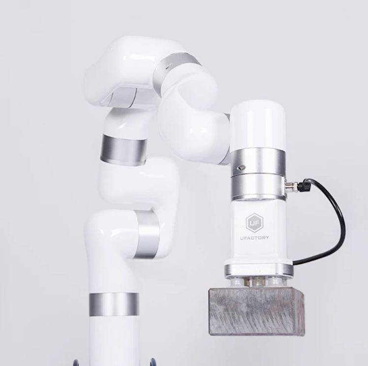 A white, multi-jointed robotic arm lifts a rectangular metal block.