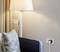 A cosy living area with an armchair, a standard lamp and a power socket. A cushion is resting on the armchair.