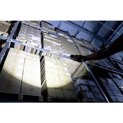 A person is illuminating a row of stacked boxes in a large storage room with a torch.