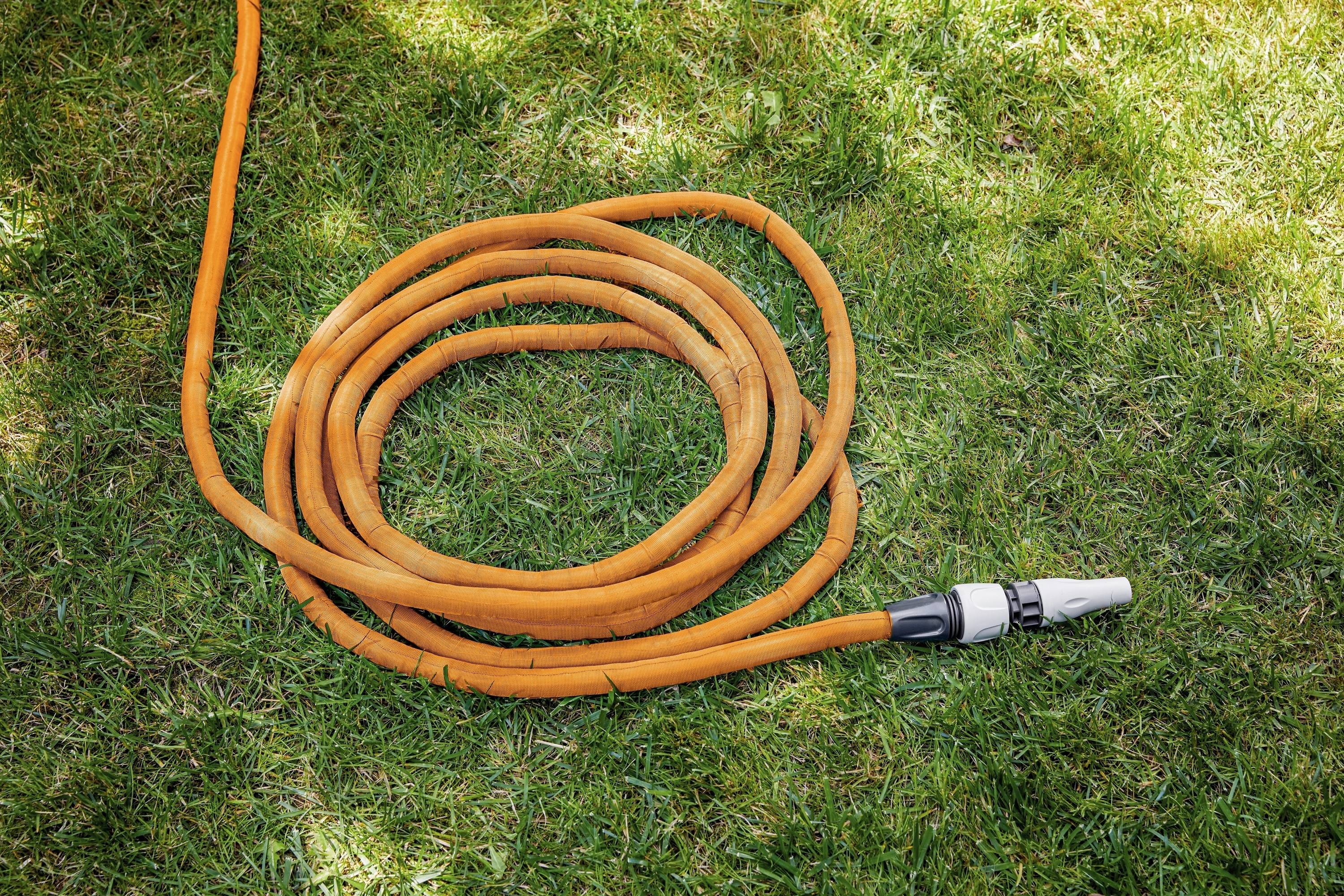 An orange garden hose lies in several coils on green grass, ready for watering.