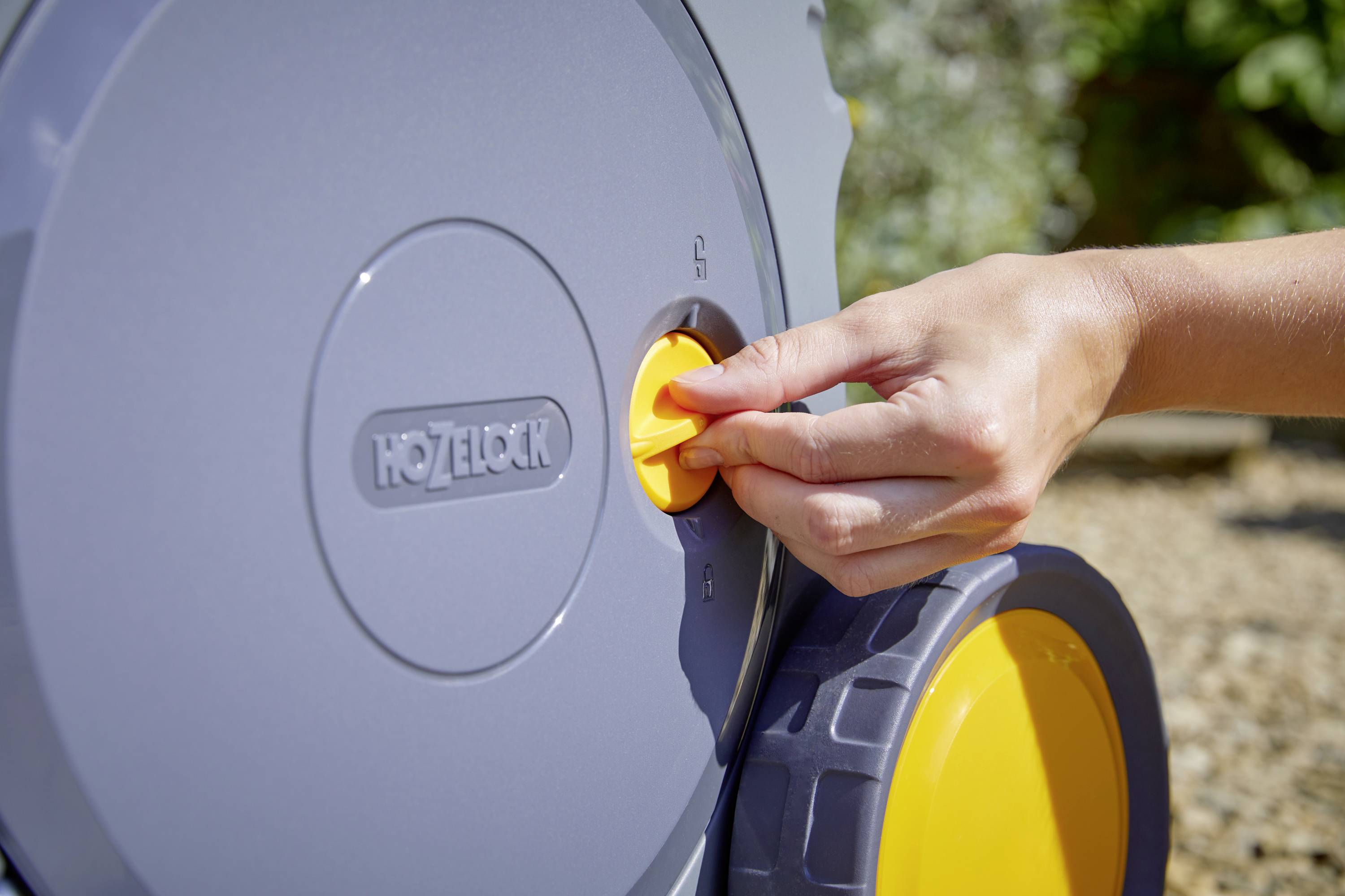 A hand is turning a yellow knob on a grey garden hose reel.