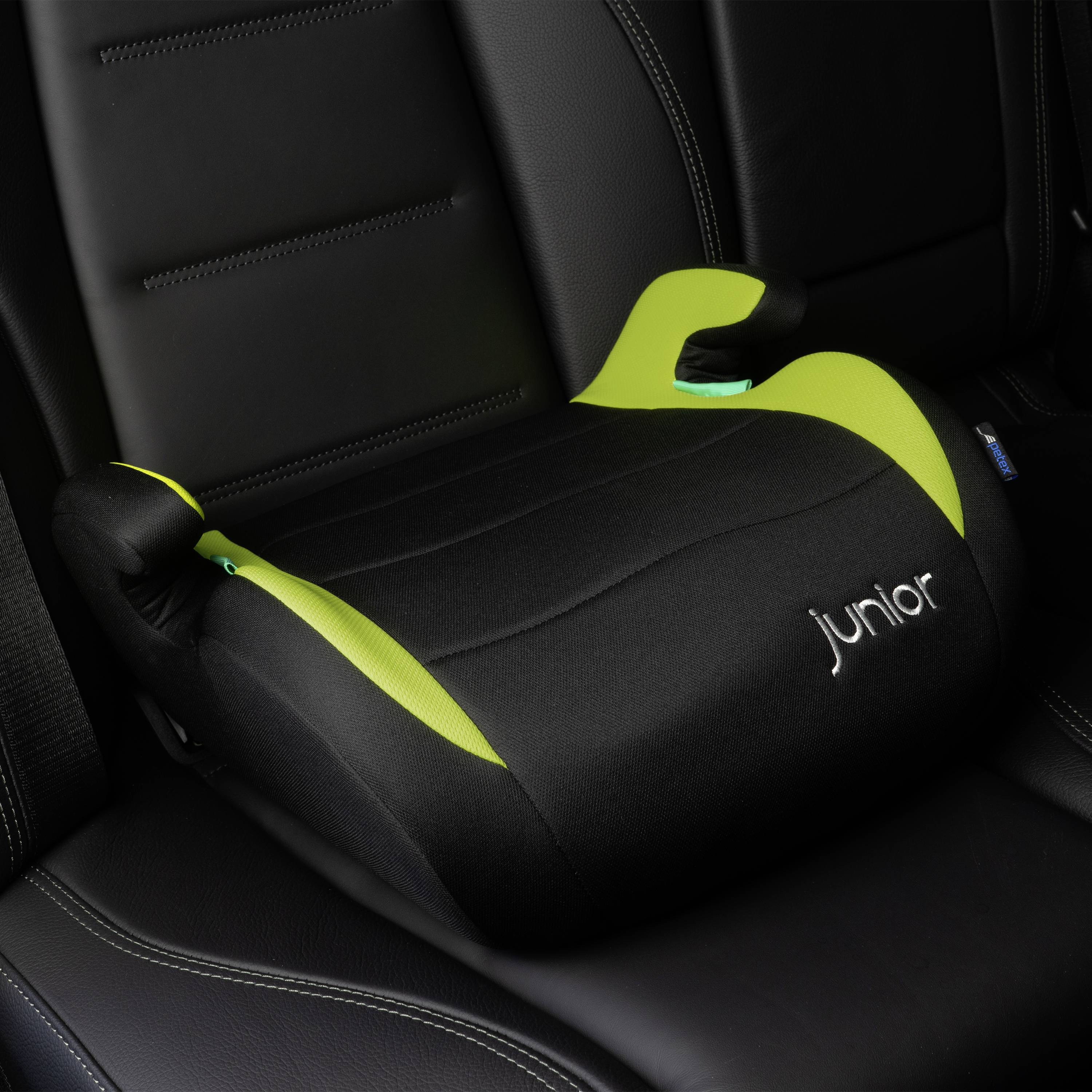 Booster seat 'Junior' placed on car seats, in black with green accents and armrests.