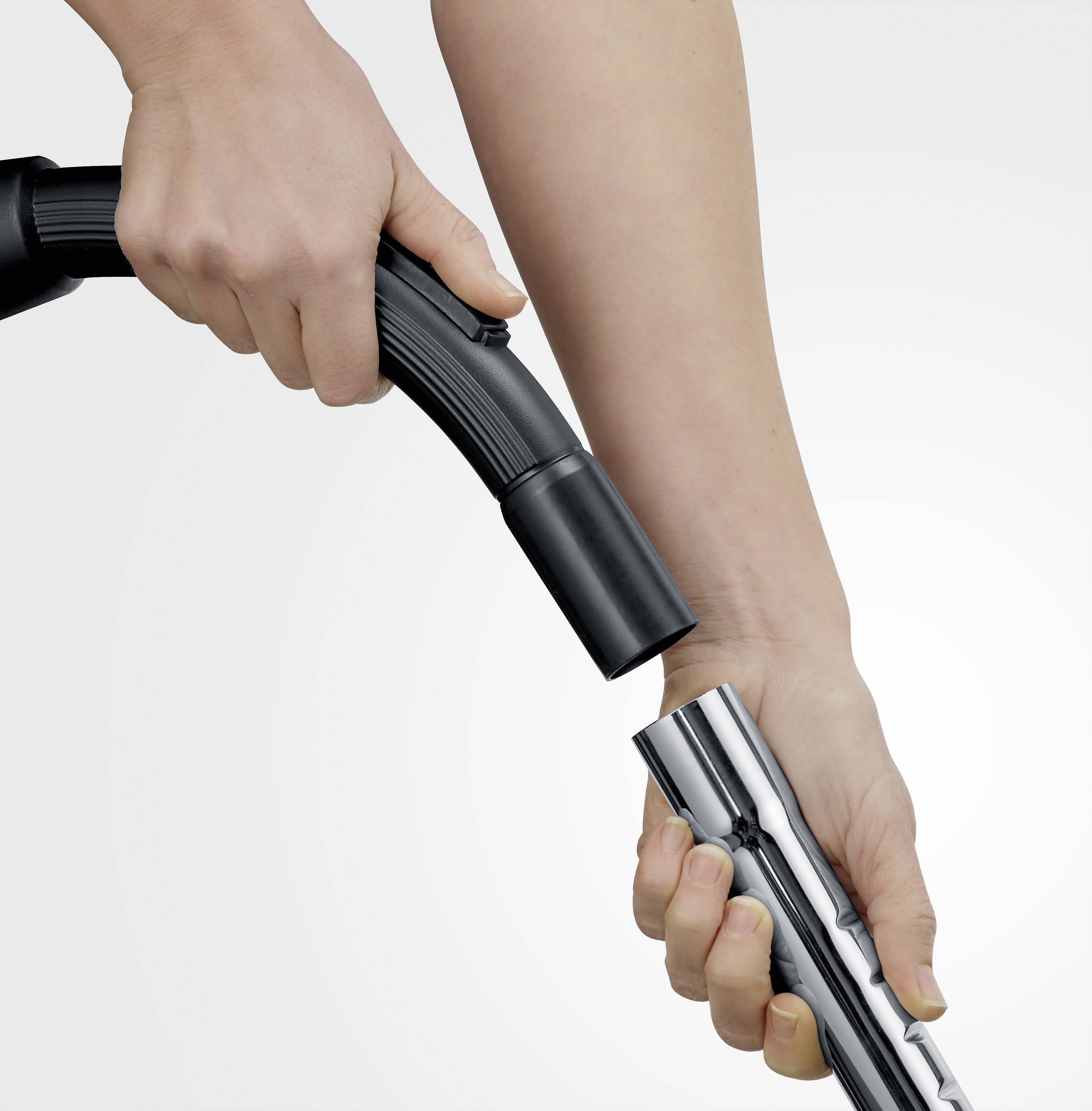 A person is holding a vacuum cleaner hose and connecting it to a metal pipe. Hands-on operation of a household appliance.