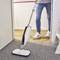 A person is using a steam cleaner on a carpet. The floor cleaner has a modern design and is in operation, while the person is wearing jeans and trainers.