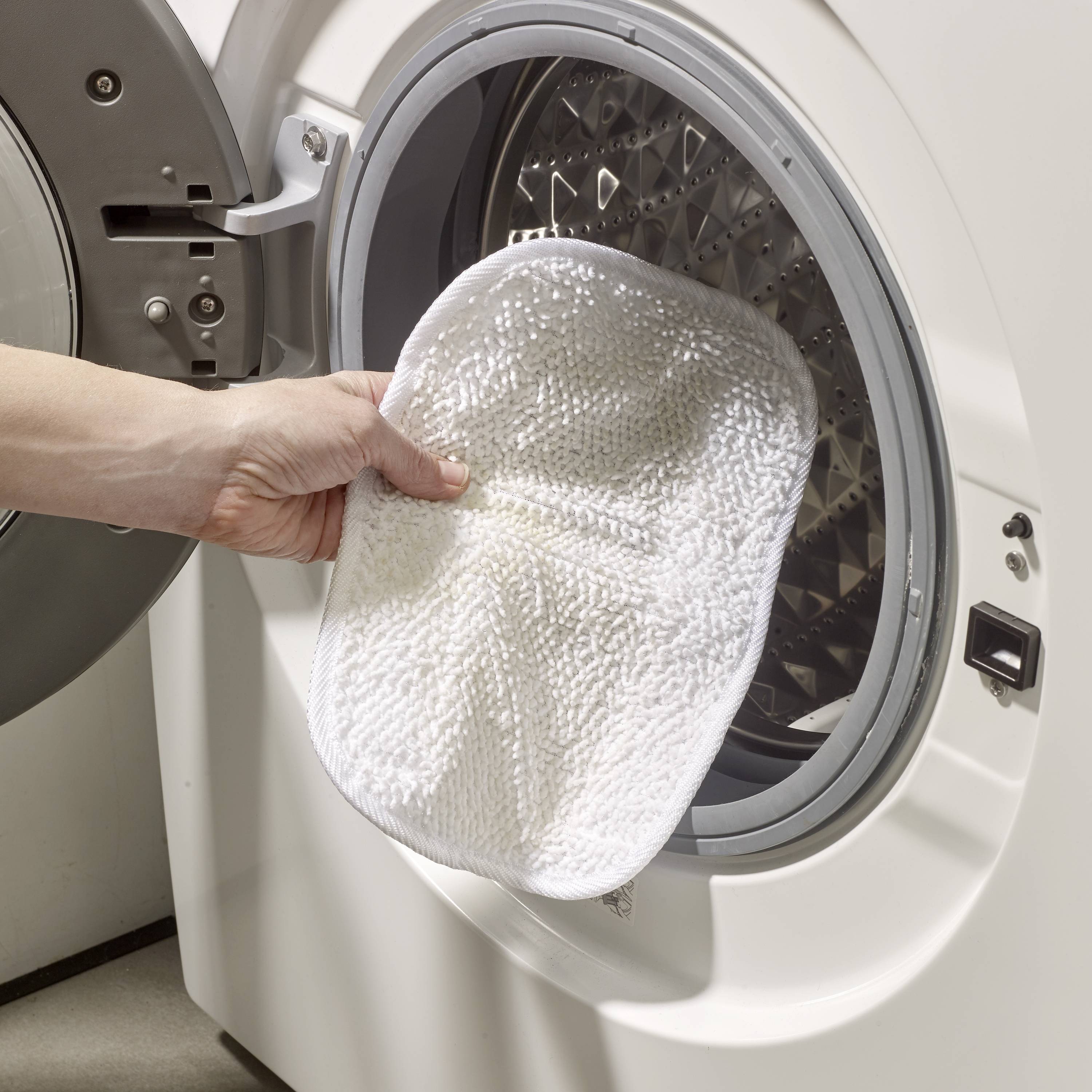 A hand places a dirty cloth into an open washing machine. The scene depicts an everyday household chore.