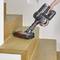 A cordless vacuum cleaner is cleaning a wooden staircase. One hand is holding the vacuum cleaner handle, while the brush moves over the steps.