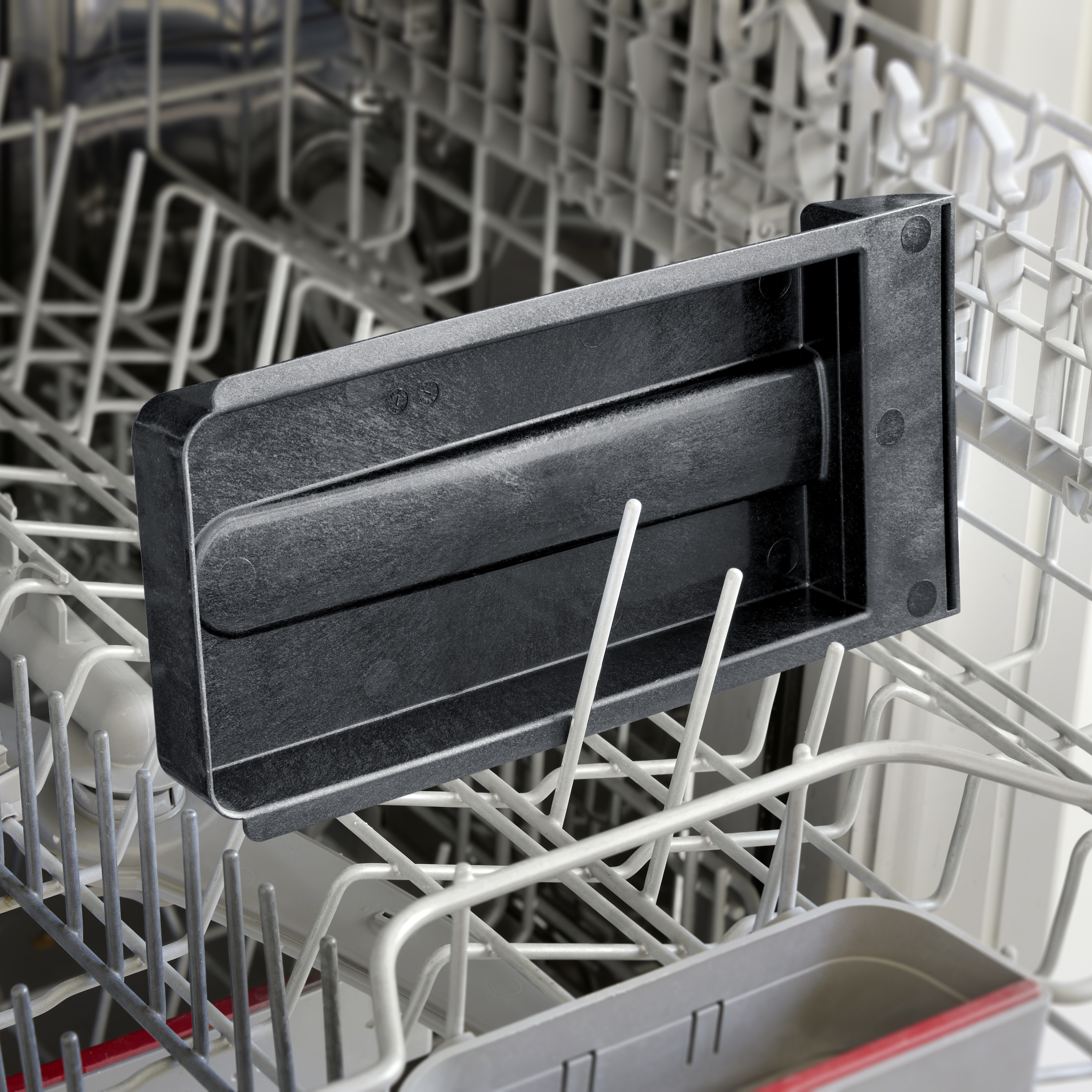 A black plastic object placed on the bottom rack of an opened dishwasher. It demonstrates a simple design.