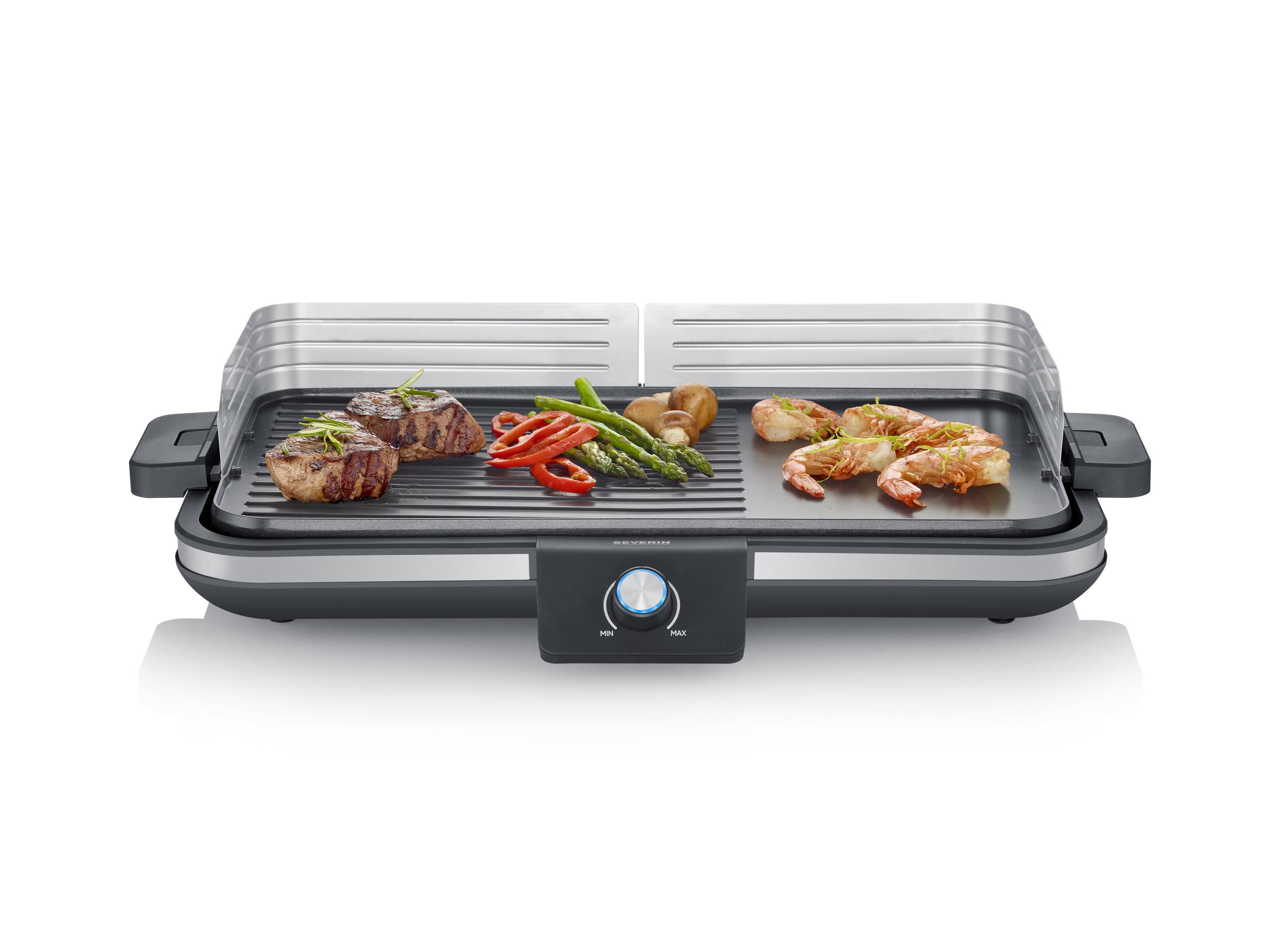 An electric tabletop grill with grilled meat, prawns, peppers, asparagus and mushrooms on the grill plate.
