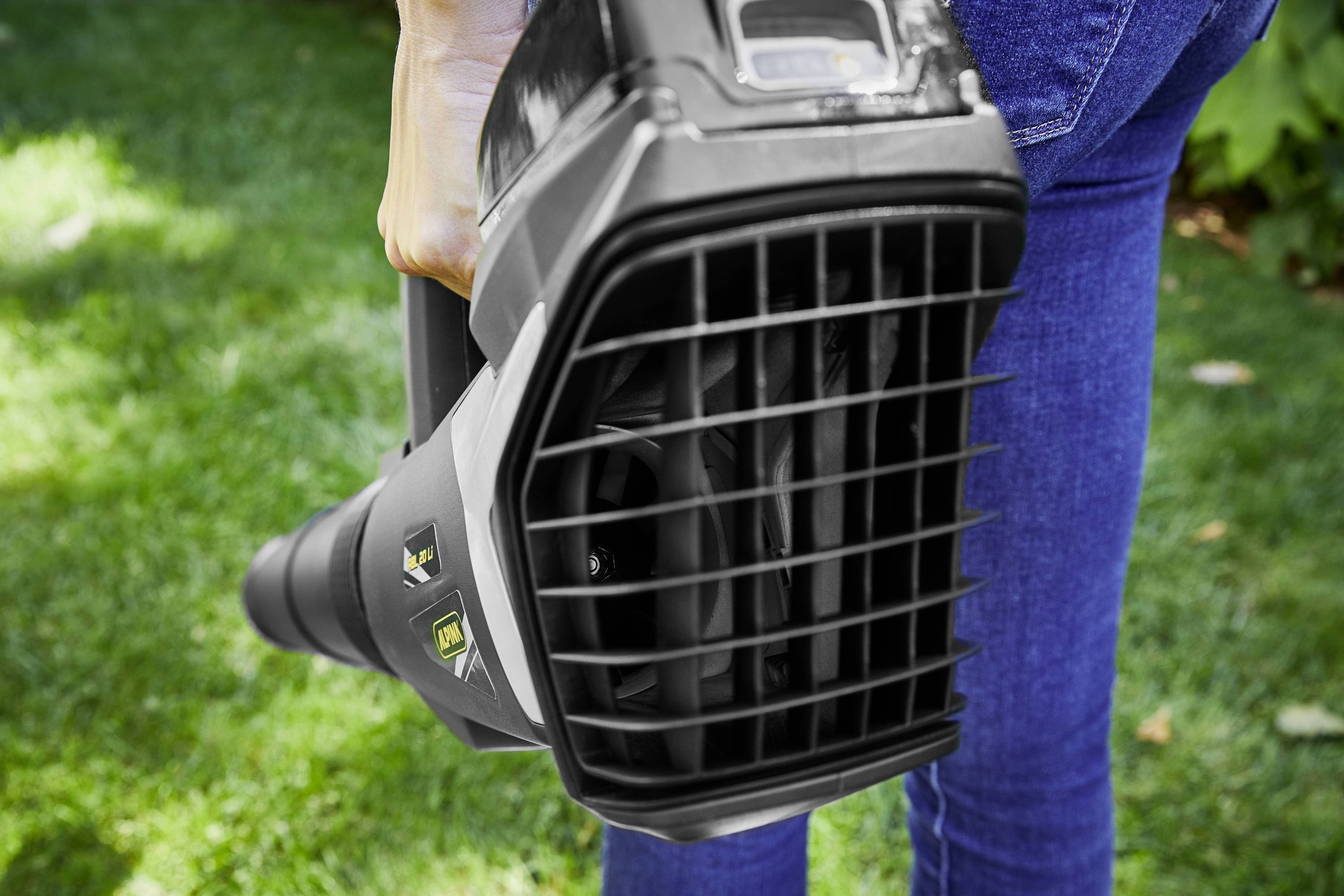 A person is holding a leaf blower hovering over a green lawn, ready for use.