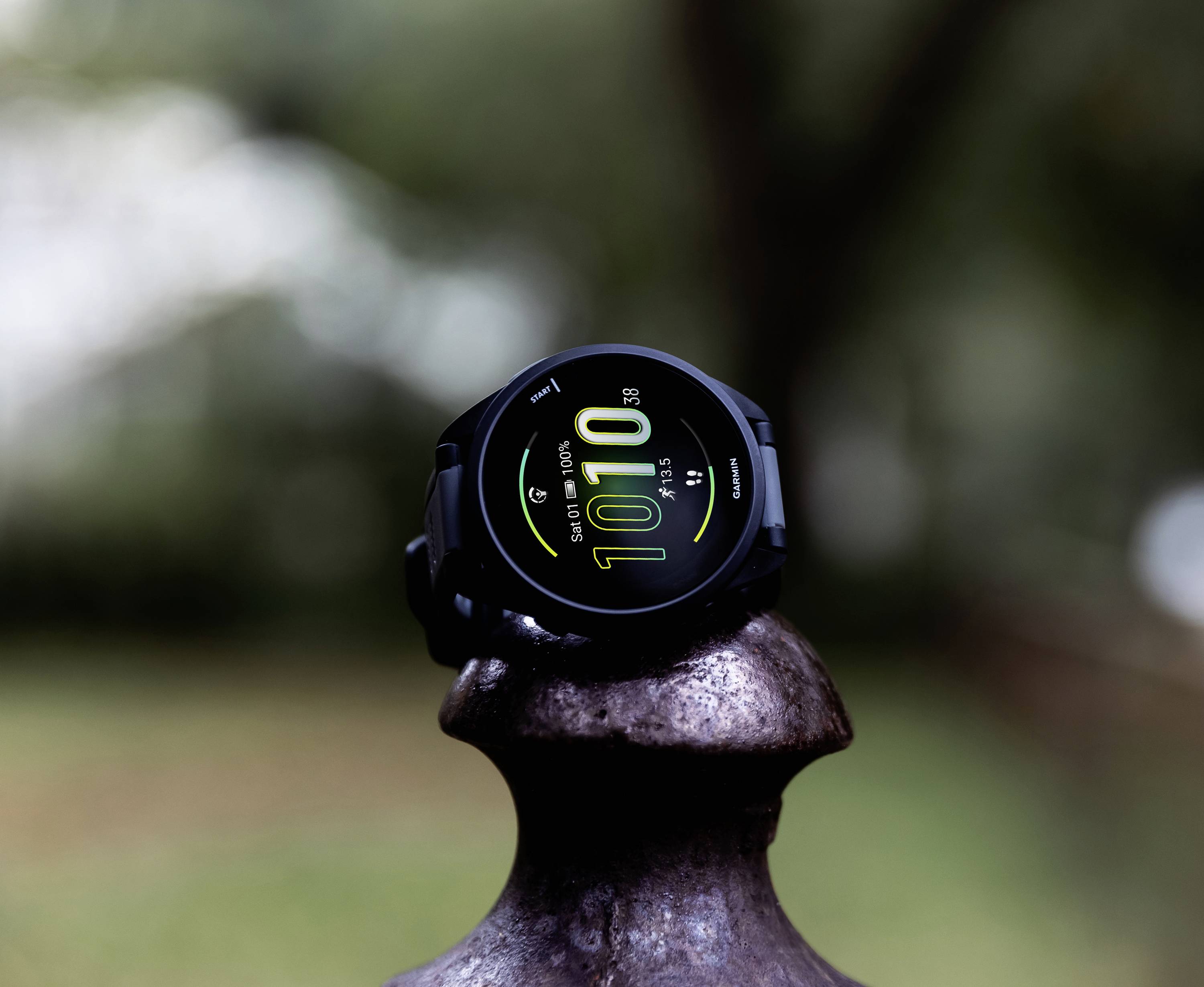 A black smartwatch displays the time '10:10', date, and heart rate information on a blurred background.