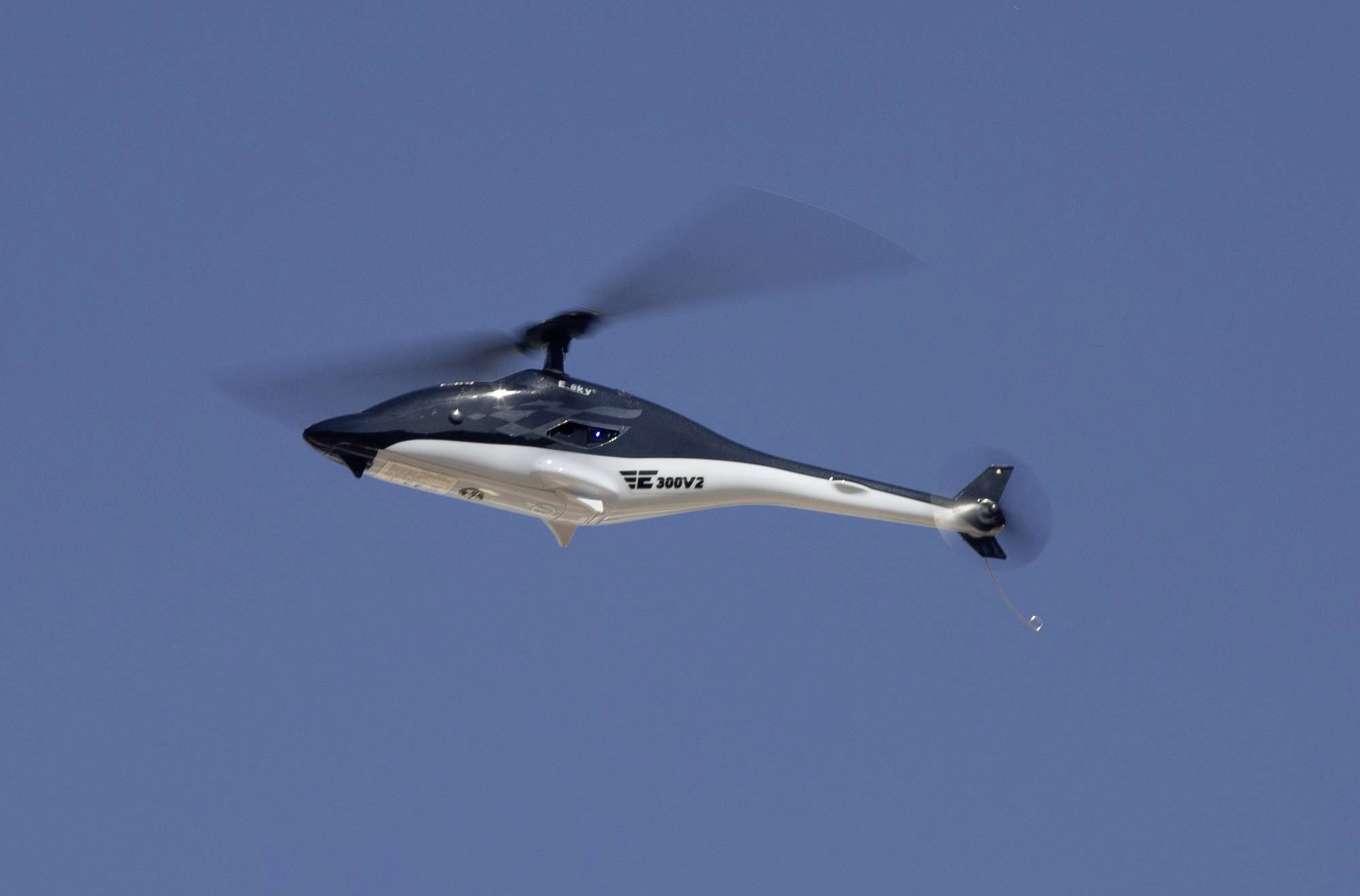 A modern rotary aircraft flies in a clear blue sky, its sleek lines and futuristic design clearly visible.