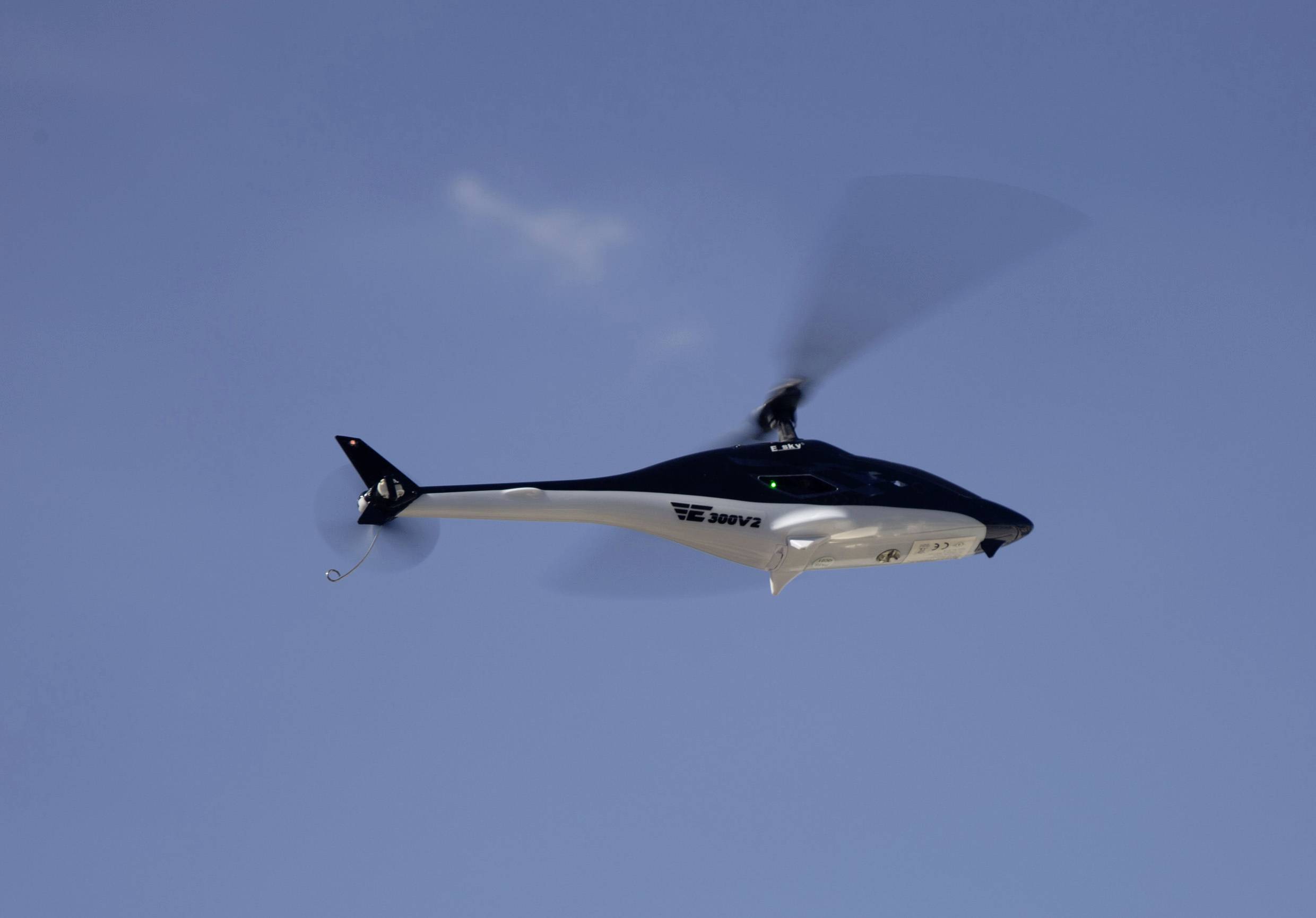 A black helicopter flies in the blue sky.