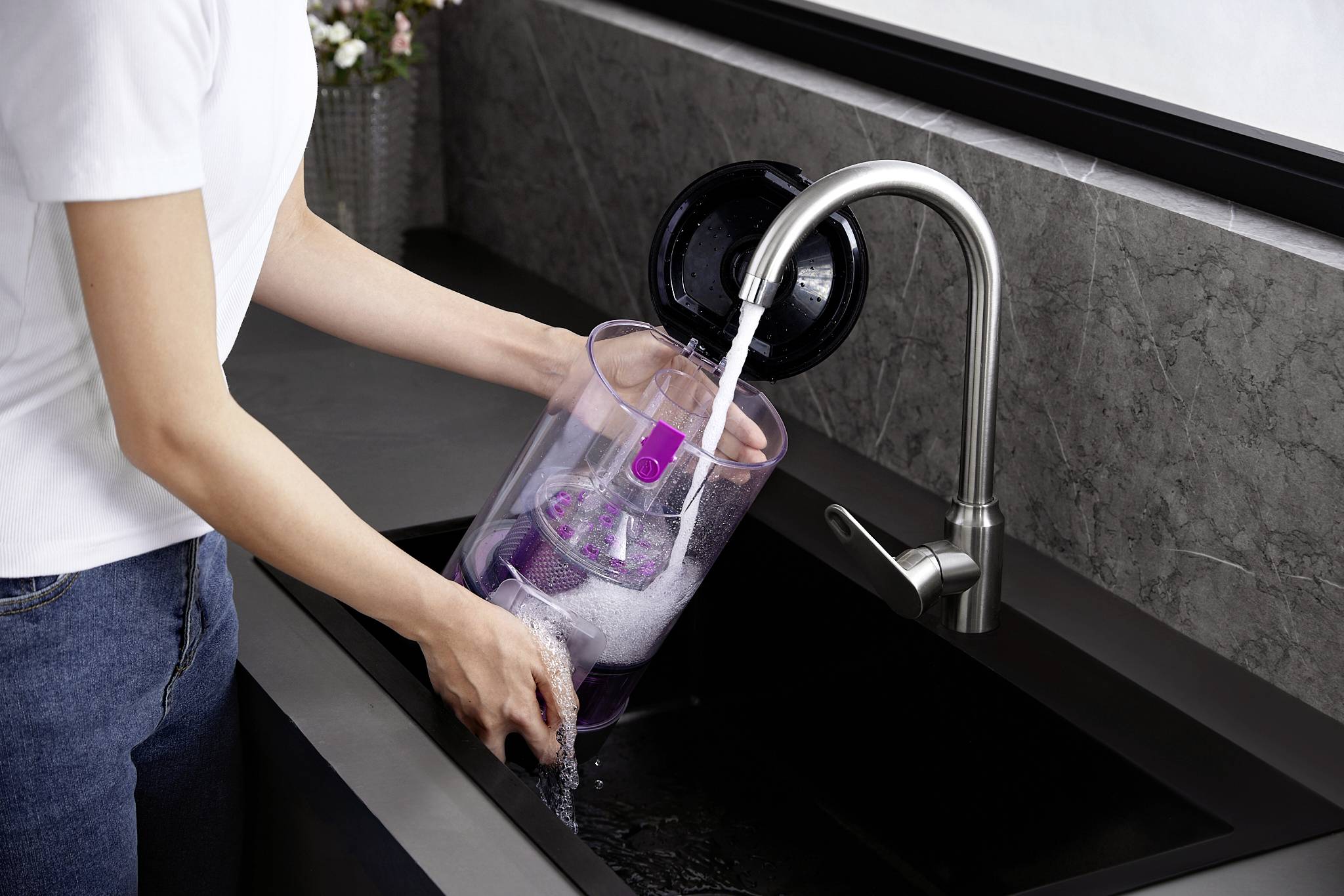 A person is filling a transparent container with water from a tap in a modern kitchen.
