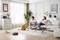 A couple sits on a sofa in a modern living room, with a dog sitting opposite them. A robotic hoover is in operation.
