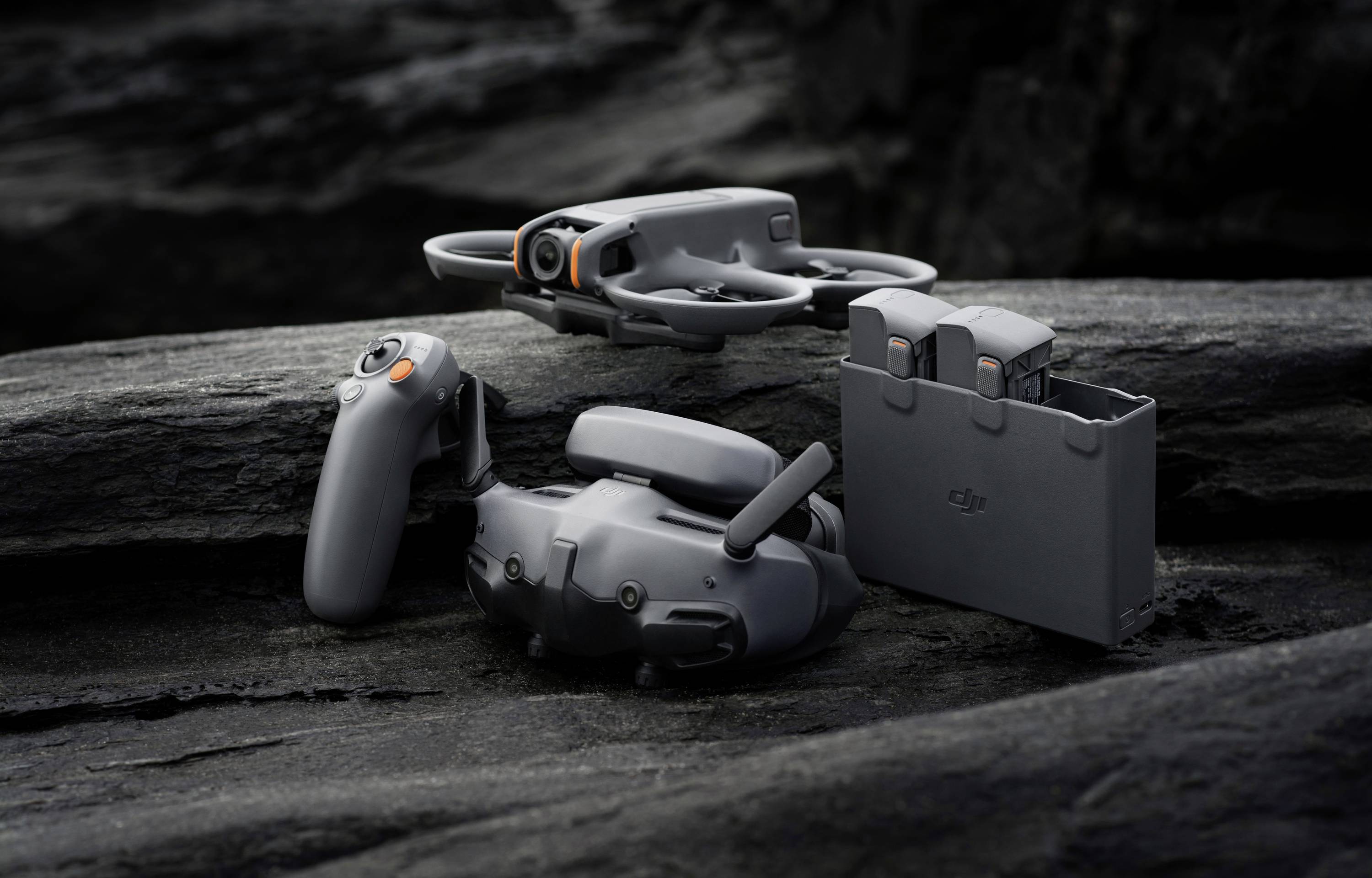 Remote-controlled drone with two spare batteries on rocky ground, ready for flight.