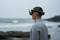 A person stands by the sea wearing a virtual reality headset. The background shows waves and a cloudy sky.
