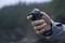 A hand is holding a grey handle with a trigger button, surrounded by a blurred, natural background.