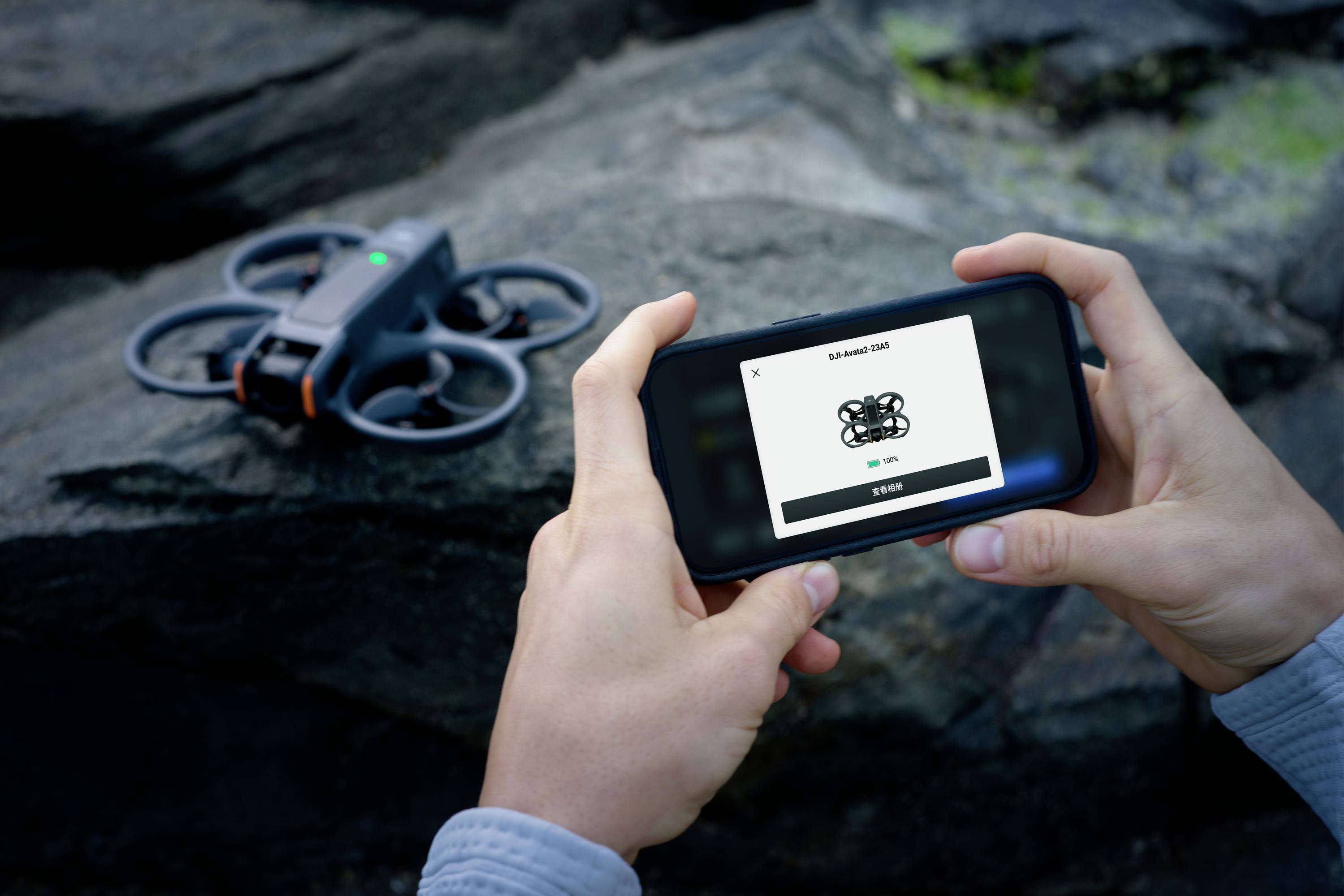 A person is holding a smartphone with a drone control app, while a drone stands on a rock. The app displays 'SCANNING 20%'.