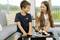A boy and a girl are sitting on a sofa, smiling and looking at each other. In front of them, a toy helicopter sits on a table.