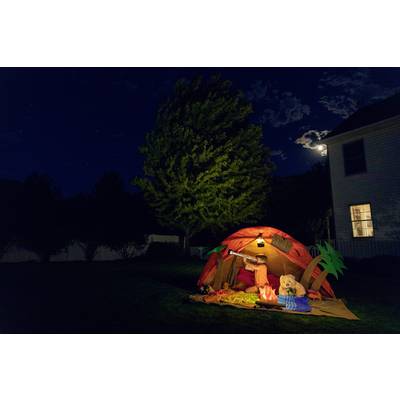 A illuminated tent in the garden at night, with a child lying in the tent using binoculars. The moon is partially visible.