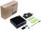 Small, black industrial computer with accessories including power supply, green mounting plates, and screws. Packaging box in the background.