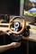 A person is mounting an orange gaming steering wheel on a desk in front of two monitors.