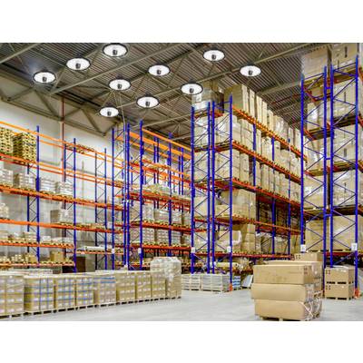 A large warehouse with tall shelving, filled with boxes and parcels. Bright industrial lighting and pallets on the floor.