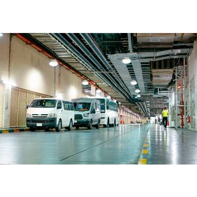Several white delivery vans are parked in a long row in an underground car park. A person is walking in the distance.