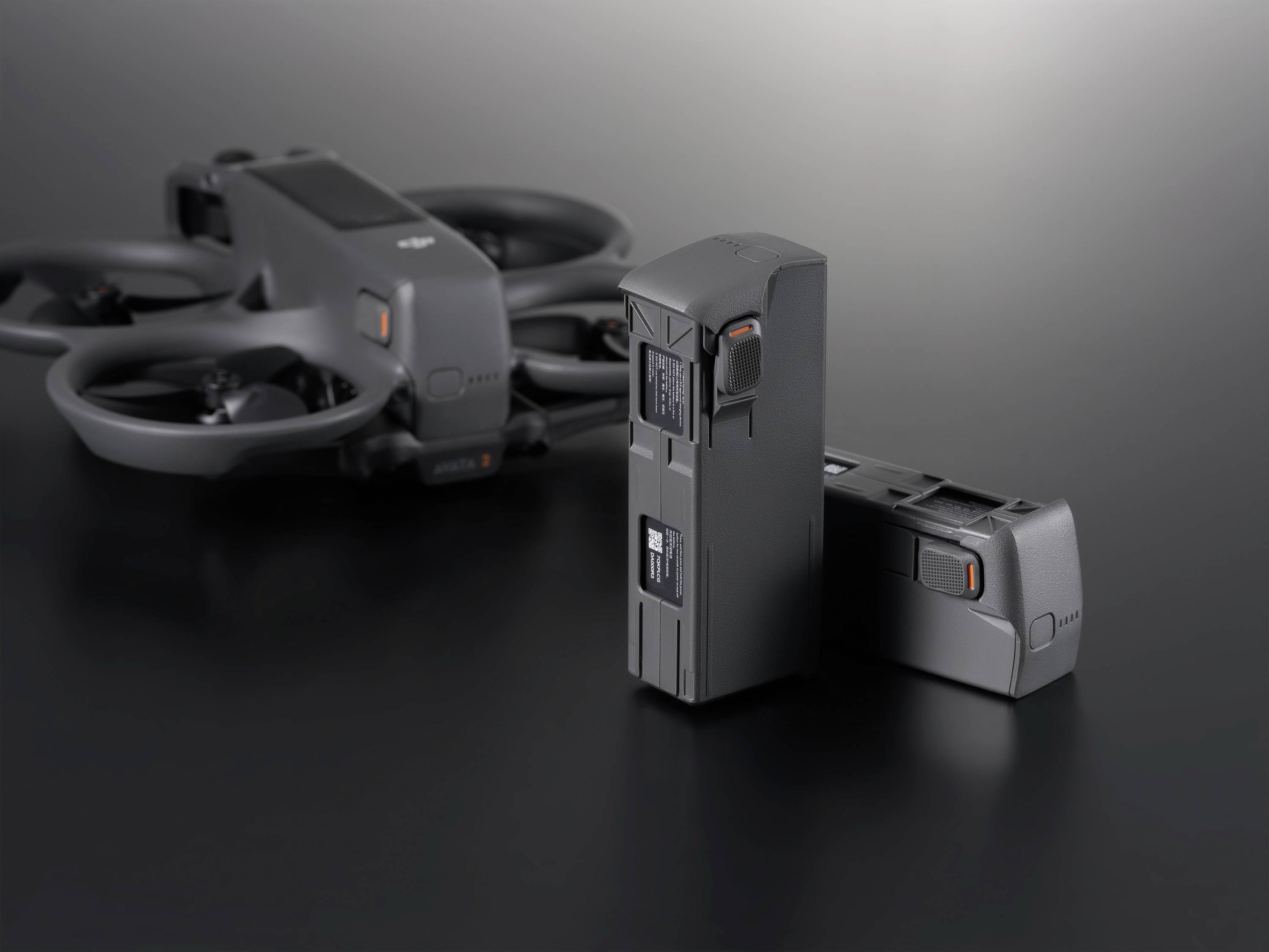 A black drone and two batteries are sitting on a dark table. The drone has protective propeller guards.