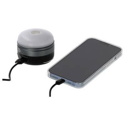 A smartphone is charging via a cable connected to a small portable power bank with a domed top.<br>