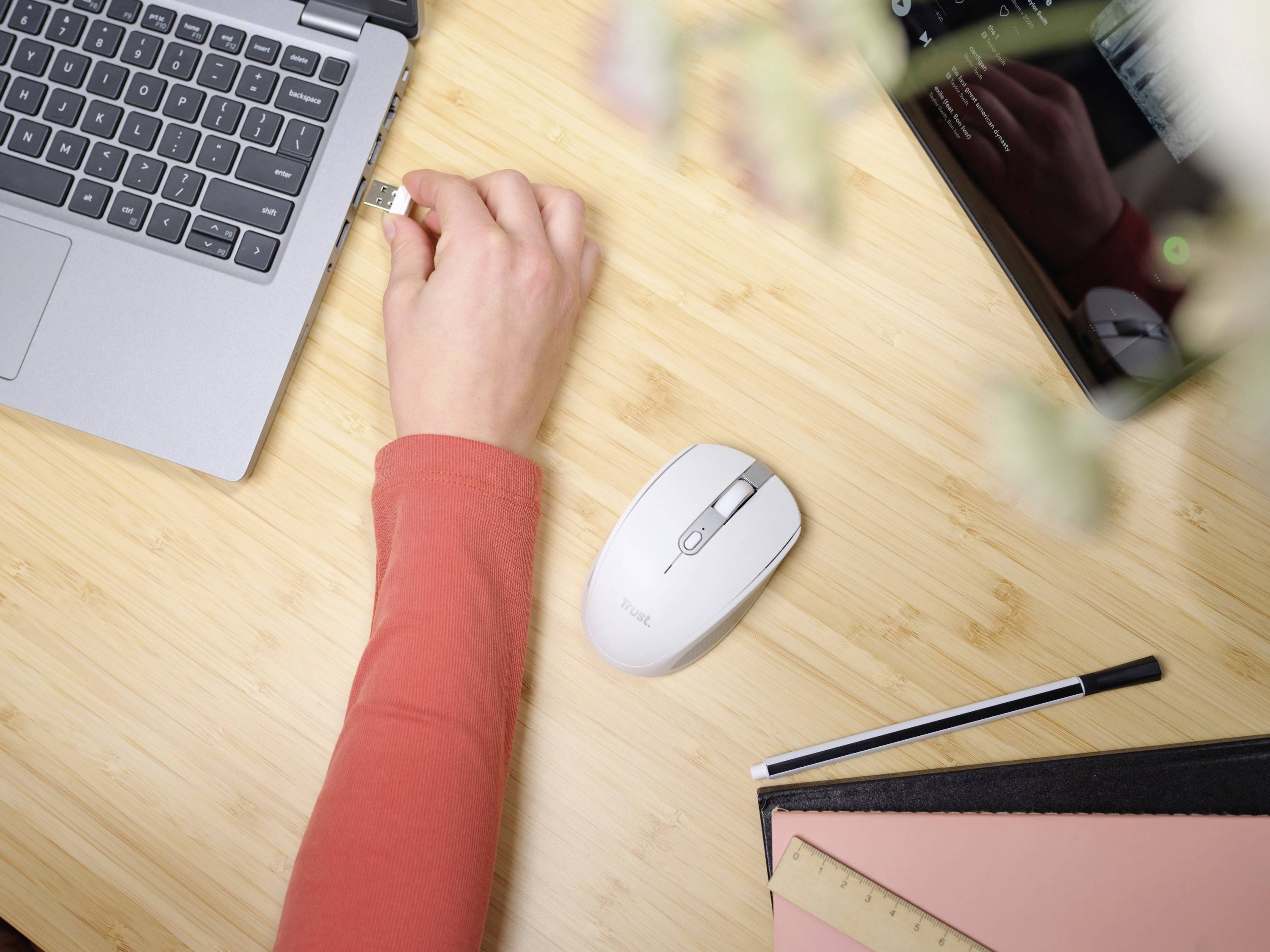 A hand is inserting a USB stick into a laptop on a wooden table. Beside it are a mouse, a tablet, a pen and a notebook.